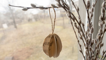 ON the branches of a willow with soft buds hang eggs made of paper. Eggs made of paper at Easter hang on willow branches with buds. Decorations for the house for the Easter holiday.の写真素材