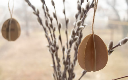 Eggs made of paper at Easter hang on willow branches with buds. Decorations for the house for the Easter holiday. ON the branches of a willow with soft buds hang eggs made of paper.の写真素材