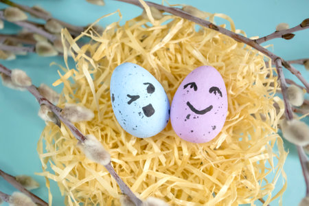 Two eggs with emoji in the nest. Festive eggs in a nest among the branches on a blue background. Emoticons on eggs for Easter.の写真素材