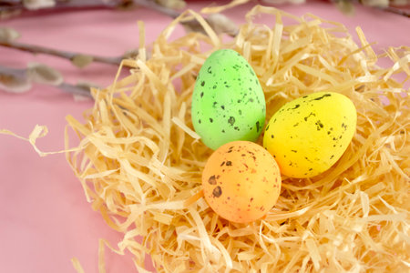 Against a pink background lie painted easter eggs in a nest next to willow branches. Easter composition - eggs in the nest. Small quail eggs are painted. Colored eggs in the nest.の写真素材
