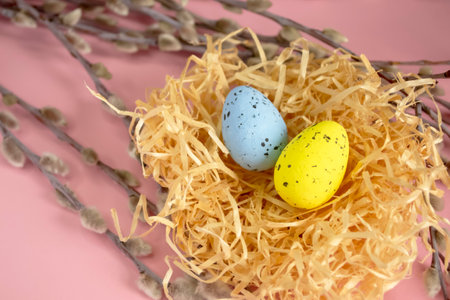Against a pink background lie painted easter eggs in a nest next to willow branches. Easter composition - eggs in the nest. Colored eggs in the nest. Small quail eggs are painted.の写真素材