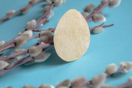 On a blue background are willow branches and one paper egg. Crafts for Easter with your own hands. Eggs for Easter from paper. Beautiful composition for Easter.の写真素材