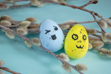 Two colored eggs for Easter lie on a blue background next to willow branches. Soft buds on the willow, decorated Easter eggs emoji. decorations for Easter.の写真素材