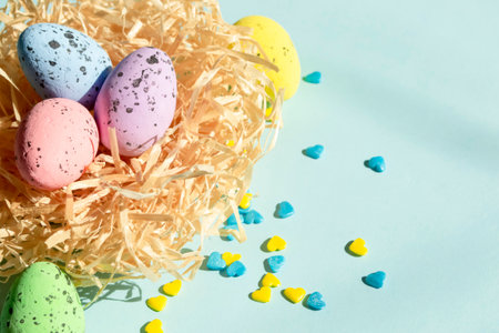 On a blue background lies a nest with Easter eggs, and next to yellow and blue hearts. Delicious quail eggs layer coloring for Easter in the nest. Decorations for Easter.の写真素材