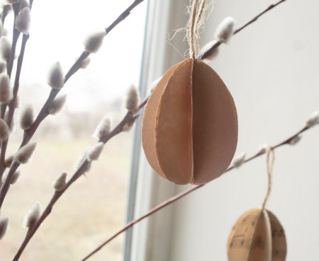 Eggs made of paper at Easter hang on willow branches with buds. Decorations for the house for the Easter holiday. ON the branches of a willow with soft buds hang eggs made of paper.の写真素材