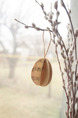 ON the branches of a willow with soft buds hang eggs made of paper. Eggs made of paper at Easter hang on willow branches with buds. Decorations for the house for the Easter holiday.の写真素材