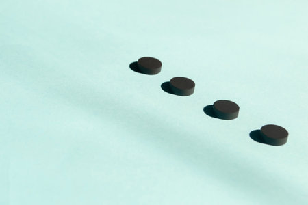 Four black pills lie in a row on a blue background. black pills. Graphic photo - lines of shadows from sunlight.の写真素材