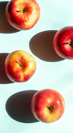 On a blue background lie red apples with yellow barrels. Bright sunlight falls on the apples creating a contrasting shadow.の写真素材