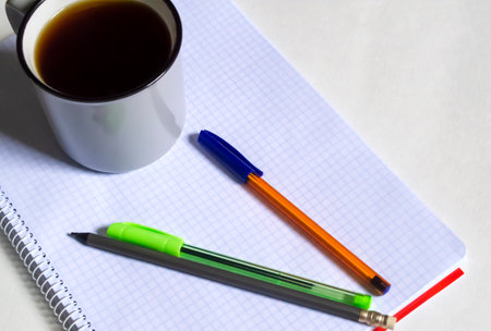 A cup of coffee next to the notepad and pens. On the table is a plaid notebook, three pens and a cup of black coffee. Americano during his studies.の写真素材