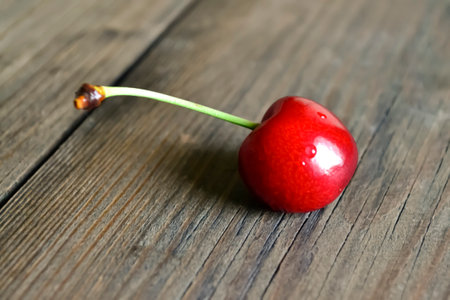 One cherry berry lies on a wooden table. A berry with a green tail. Big cherry. A large red berry on the table. Summer berries.の写真素材
