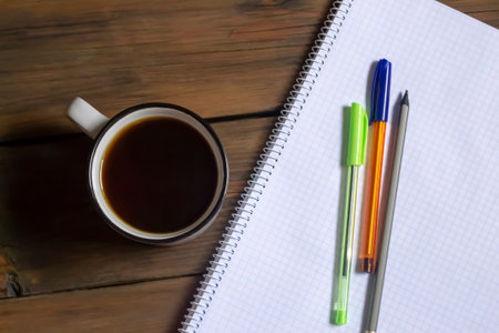 A cup of coffee next to the notepad and pens. Americano during his studies. On the table is a plaid notebook, three pens and a cup of black coffee.の写真素材