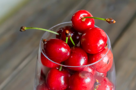 Cherries in a glass. In the glass are red cherry berries. On a wooden background is a glass with berries. Summer berries are a healthy food. fresh cherry juice.の写真素材