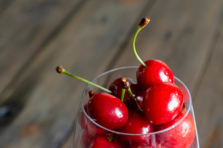Cherries in a glass. On a wooden background is a glass with berries. In the glass are red cherry berries. Summer berries are a healthy food. fresh cherry juice.の写真素材