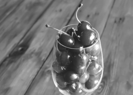 Cherries in a glass. Black and white photo. On a wooden background is a glass with berries. Summer berries are a healthy food. fresh cherry juice.の写真素材