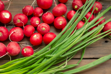 Radish lies next to green onions on a wooden table. Spring vegetables for salad. Useful crops in early spring. Seasonal vegetables in spring.の写真素材
