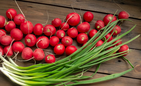 Radish lies next to green onions on a wooden table. Seasonal vegetables in spring. Spring vegetables for salad. Useful crops in early spring.の写真素材