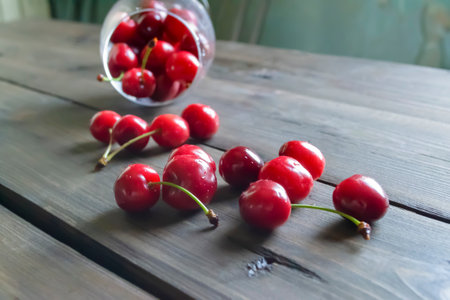 Fresh cherries in a glass. On a wooden table is a glass of cherry. Cherries spilled out of the glass onto the table.の写真素材
