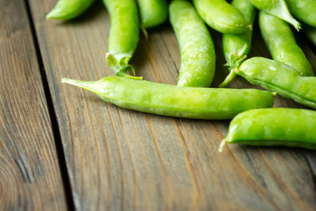 Green peas in pods lying on a wooden table. Useful legumes. The green pea pods are whole. Beans in a pod.の写真素材