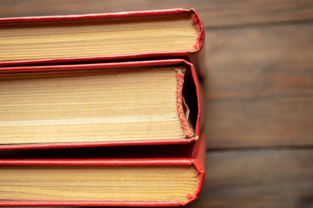 The spines of books with a red cover. Three books stand side by side on a wooden table. The end of the book is dense sheets of a closed book.の写真素材