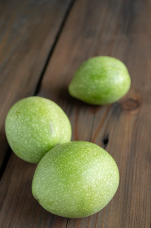 Three green walnuts on a wooden table. On a wooden background there are three walnuts in a green shell. Unpeeled nuts.の写真素材