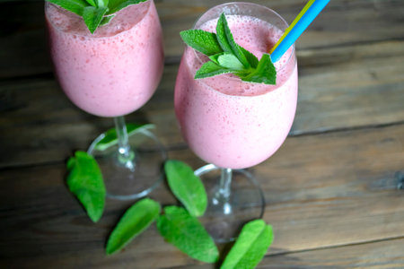 Strawberry cocktail in a glass with a straw and mint leaves. Yellow-blue straw for a cocktail. On a wooden table there is a glass with a strawberry cocktail, mint leaves.の写真素材