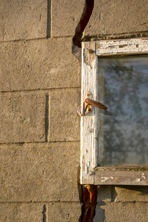An old little window in the barn. The glass window in the bar is broken. The old building is in need of repair. Wooden window frame with glass and lock.の写真素材