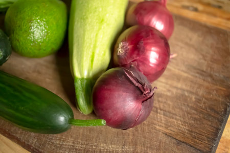 Red onion next to green vegetables. Red onion, zucchini, cabbage, cucumber and avocado on a wooden table. Vegetables in the spring.の写真素材