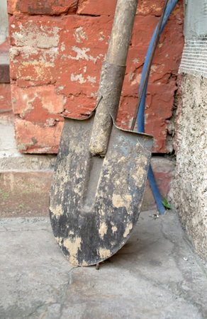 A dirty shovel stands next to the house. A dirty shovel was leaned on the wall of the house. Shovel in the ground. Caring for garden tools.の写真素材