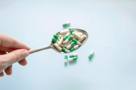In the girl's hand is a metal spoon with medical capsules. Spoon with capsules for health treatment. Taking pills with spoons is the harm and benefit of traditional medicine.の写真素材