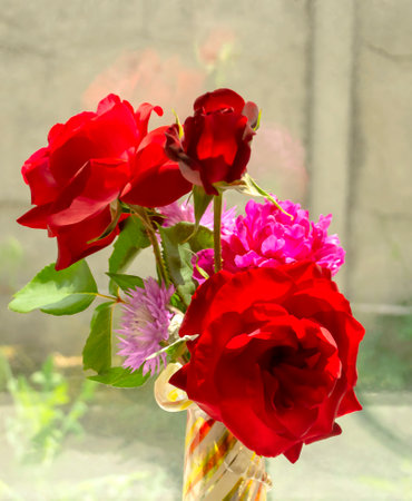 Bouquet in a vase on the window. Bouquet of roses, cornflower and peonies on the background of the window. In a vase there is a bouquet with red roses and other flowers.の写真素材