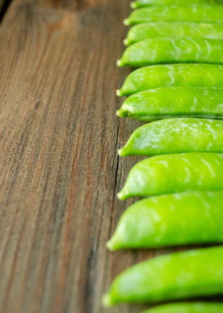 Green pea pods lie in a row on a wooden table. Green peas lie in a line. A lot of green pea pods lie flat.の写真素材