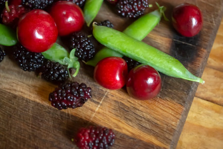 Mulberries, cherries and green peas on a wooden board. Healthy summer berries and green peas. Bright photo of summer berries. There are many summer berries on a wooden background.の写真素材