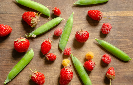 Strawberries, raspberries and green peas on a wooden board. Summer berries are health benefits. Green and red berries from the garden. Healthy breakfast.の写真素材