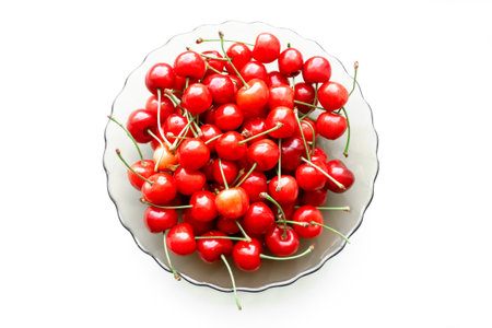 Plate with red cherries on a white background. On a white table, red cherries with green tails lie in a pile in a plate.の写真素材