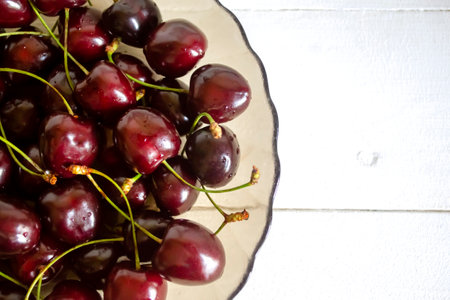 A white wooden table and a plate of dark red cherries. Dark cherries in a plate on a white wooden table.の写真素材
