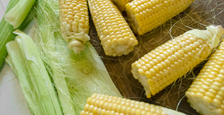 Preparation of corn - cobs with leaves on a wooden board. Young corn for cooking - harvesting...