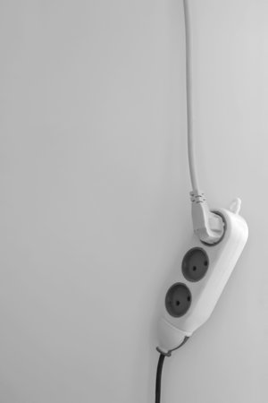 Against the background of a gray wall hangs an electric carrier with a plug turned on. Plug in the socket against the background of the wall. The carrier hangs on the included cable.の写真素材