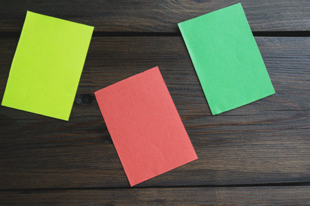 Three stickers on a wooden table. Three colored pieces of paper on the table. Red, yellow and green pieces of paper on a wooden table.の写真素材