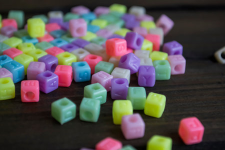 Colored cubes with letters on a wooden table. A lot of colored cubes for the bracelet on the table. Cubes with letters to create a bracelet.の写真素材