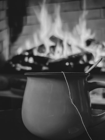 A mug of tea in front of the fireplace. Black and white photo of fireplace and cup. Cozy photo by the fireplace.の写真素材