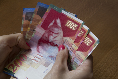 Woman holding a bunch of Israeli New Sheqel banknotes in her hands.の写真素材