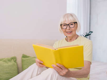 senior woman with gray hair reading a book on a sofa at home. Education, pension, anti age, reading conceptの写真素材