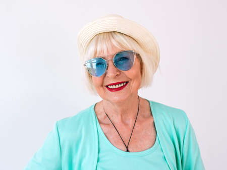 senior (old) stylish cheerful woman in straw hat and sunglasses and turquoise clothes. Summer, travel, anti age, joy, retirement, freedom conceptの写真素材