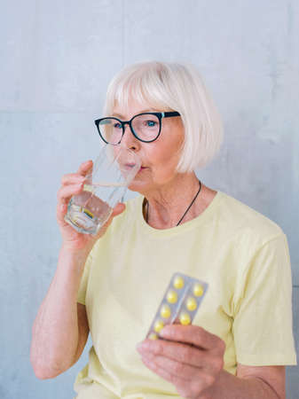 old woman in glasses holding medicine (pills) and glass of water. Age, health care, treatment conceptの写真素材