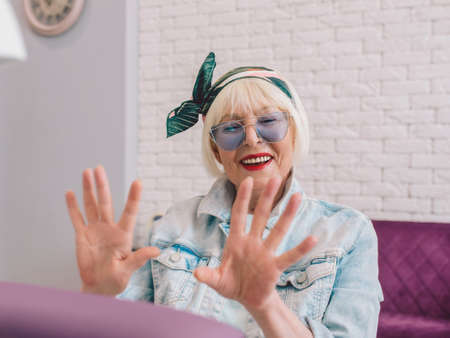 elderly stylish woman in blue sunglasses and denim jacket sitting at manicure salon (studio) happy with her nails. Treatment, care, anti age, manicure conceptの写真素材
