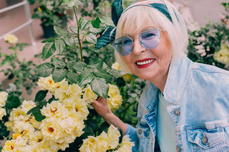 stylish senior woman in denim jacket making selfie with flowers. Gardening, traveling, positive...