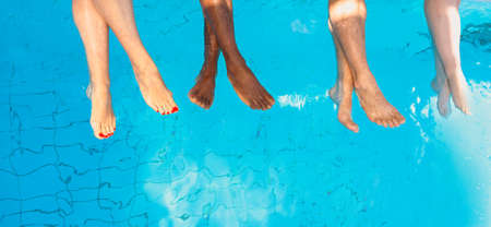 legs of four friends (common people) different race sitting by the swimming pool in sunny day....
