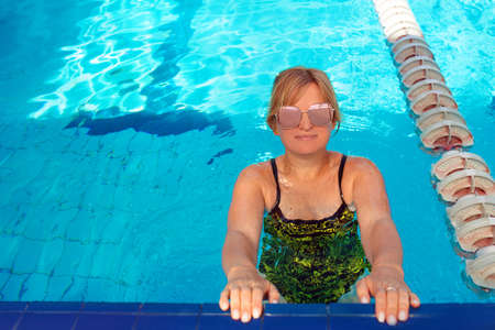 blonde woman in swimming suit and pink sun glasses by the edge in the swimming pool. Summer....