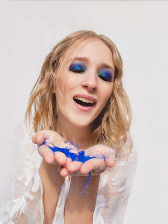 Pretty young cheerful blonde blowing blue glitter from her hands. Make up, fashion, magic, holidays,...