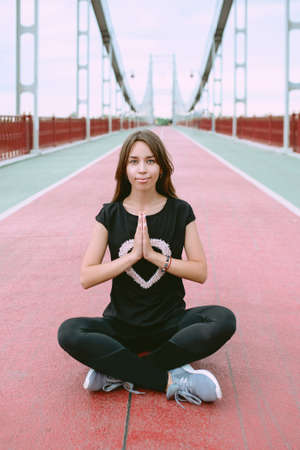 beautiful, sporty, fit, young caucasian woman in sportwear and sneakers sitting in lotus pose on the bridge. Sport, activity, yoga, urban lifestyle conceptの写真素材